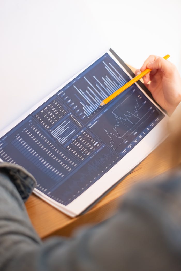 contact-img A close-up of a person analyzing blue graph data with a yellow pencil.